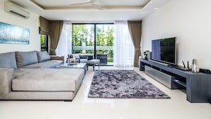 A modern living room with a grey sofa, a coffee table, a flat-screen TV, and a large window with curtains.