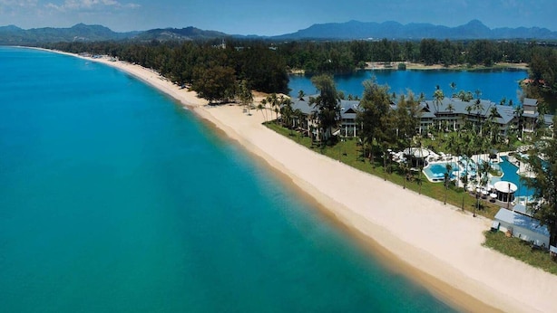 A resort with a long beachfront, clear turquoise waters, and a pool area with umbrellas.