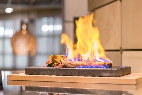 A grill with food and flames on a wooden platform.
