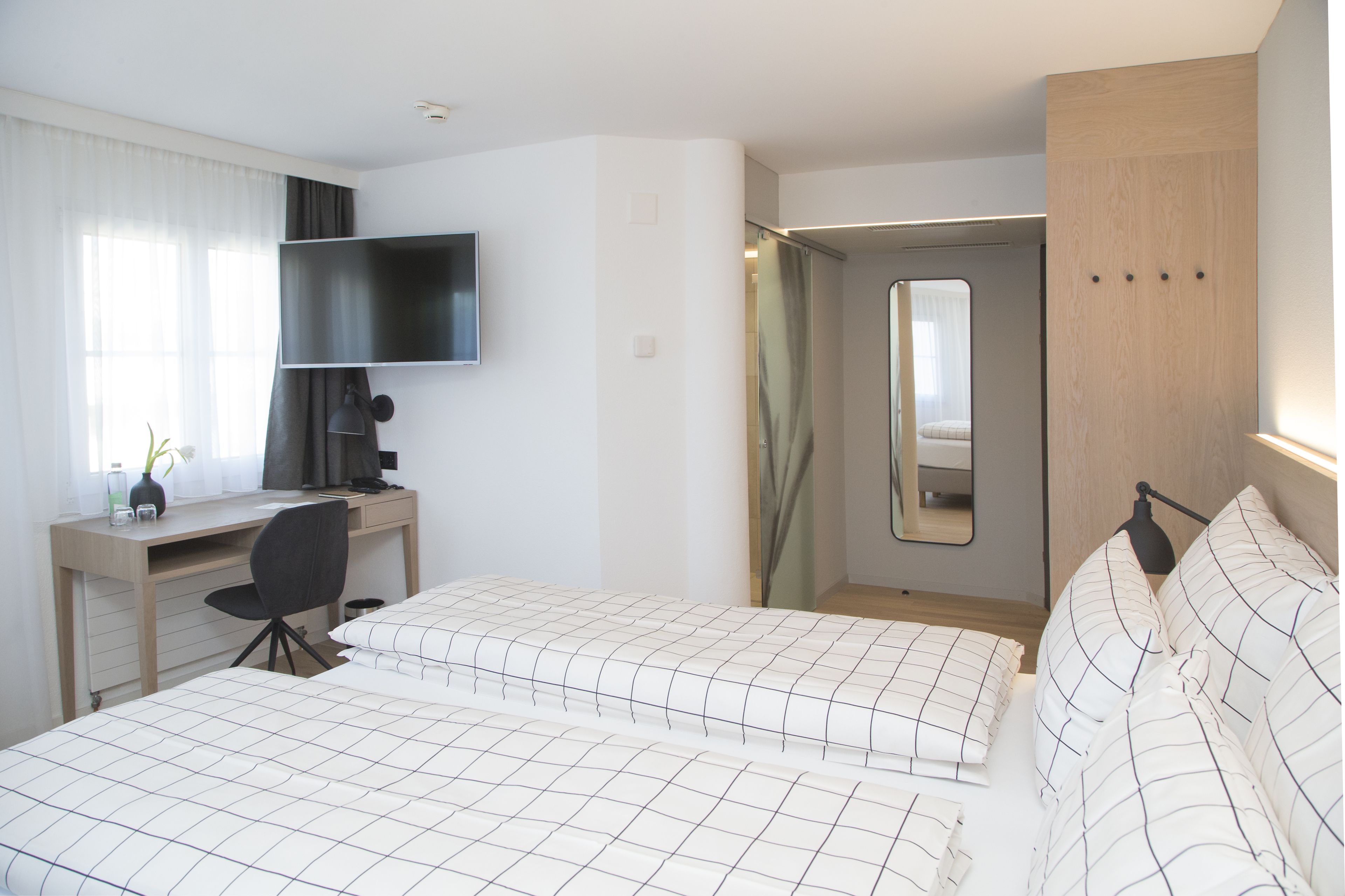 Habitación de hotel con dos camas, un escritorio, una silla, un televisor y un espejo.