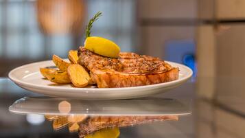 Un piatto con bistecca alla griglia, patate arrosto e spicchio di limone su una superficie riflettente.
