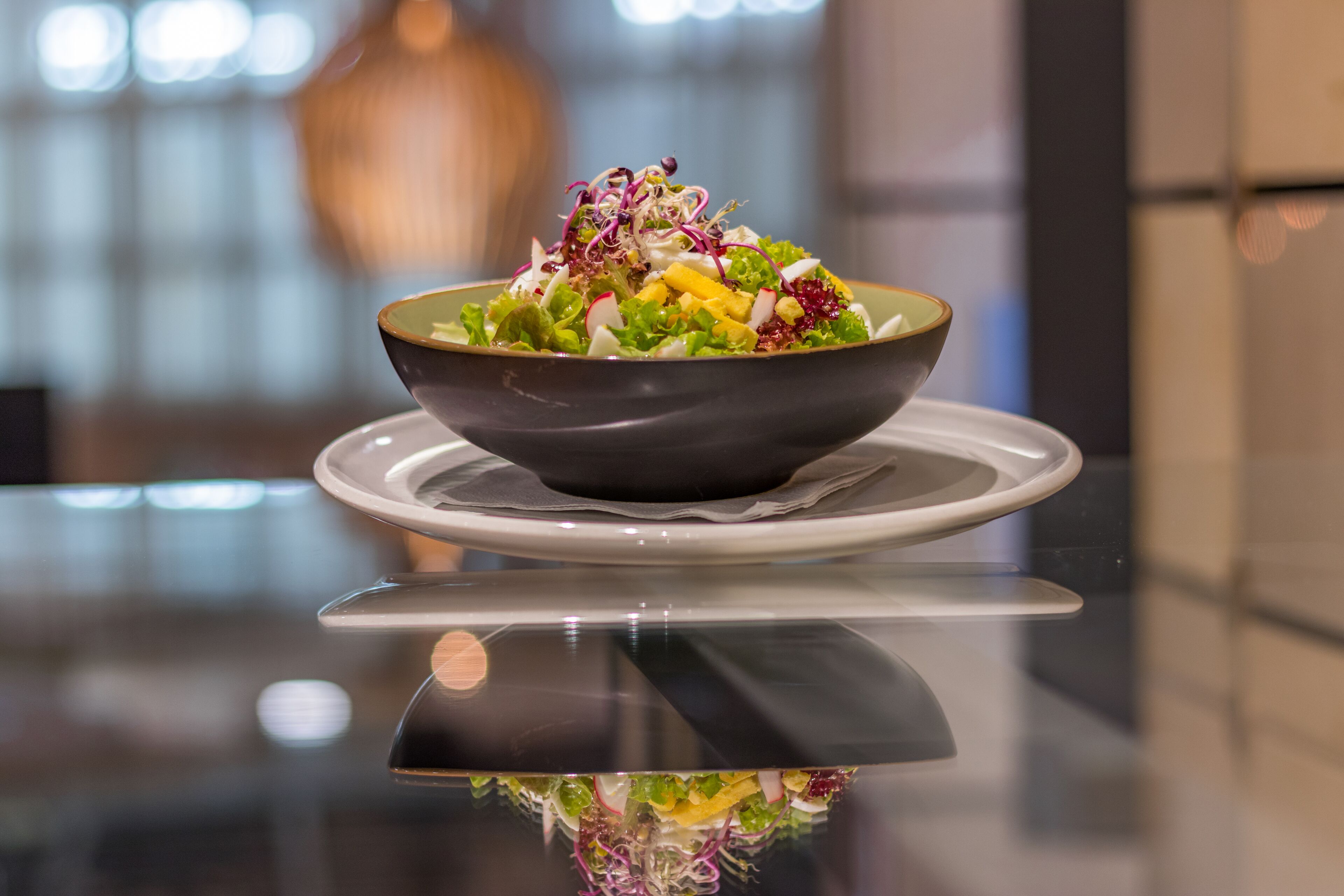 A bowl of salad on a reflective surface with a blurred background.