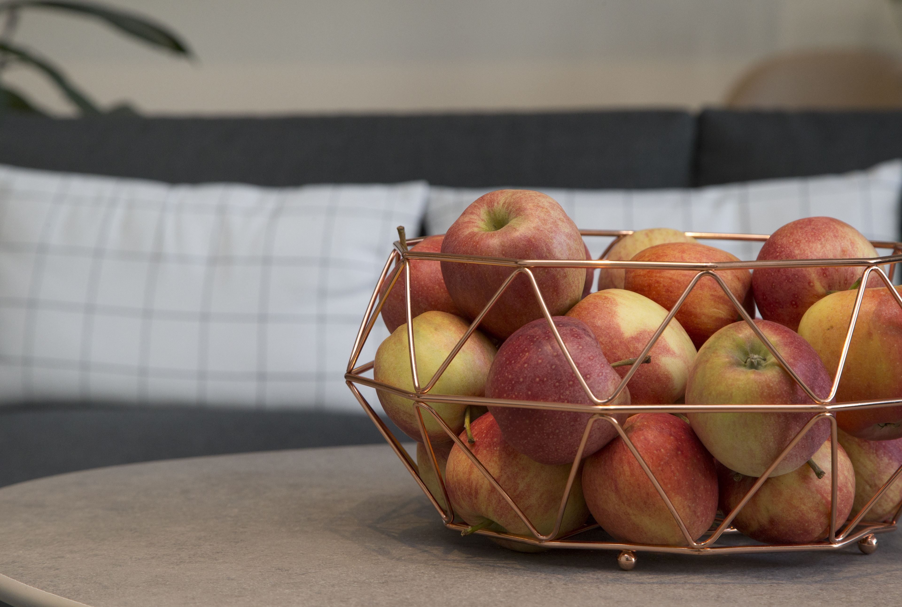Uma cesta de arame com maçãs sobre uma mesa.