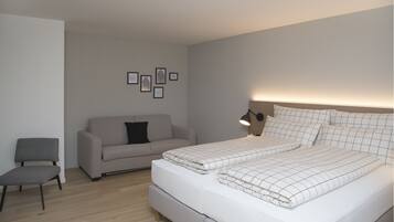 A modern bedroom with a bed, a sofa, a chair, and wall art.