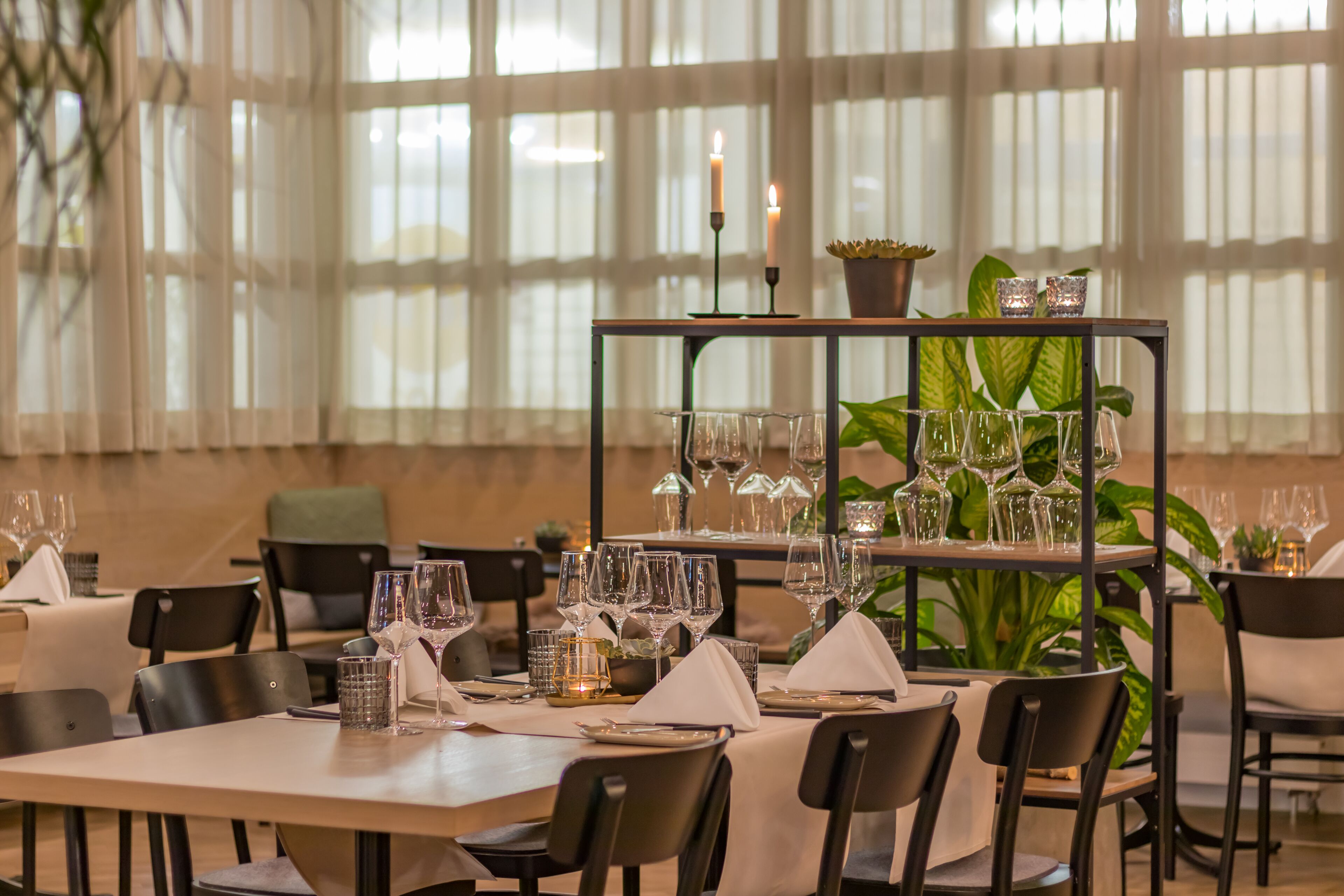 A restaurant with tables set for dining, candles, and potted plants.