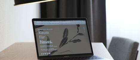 A laptop on a wooden desk with a notebook and pen beside it, under a black lamp.