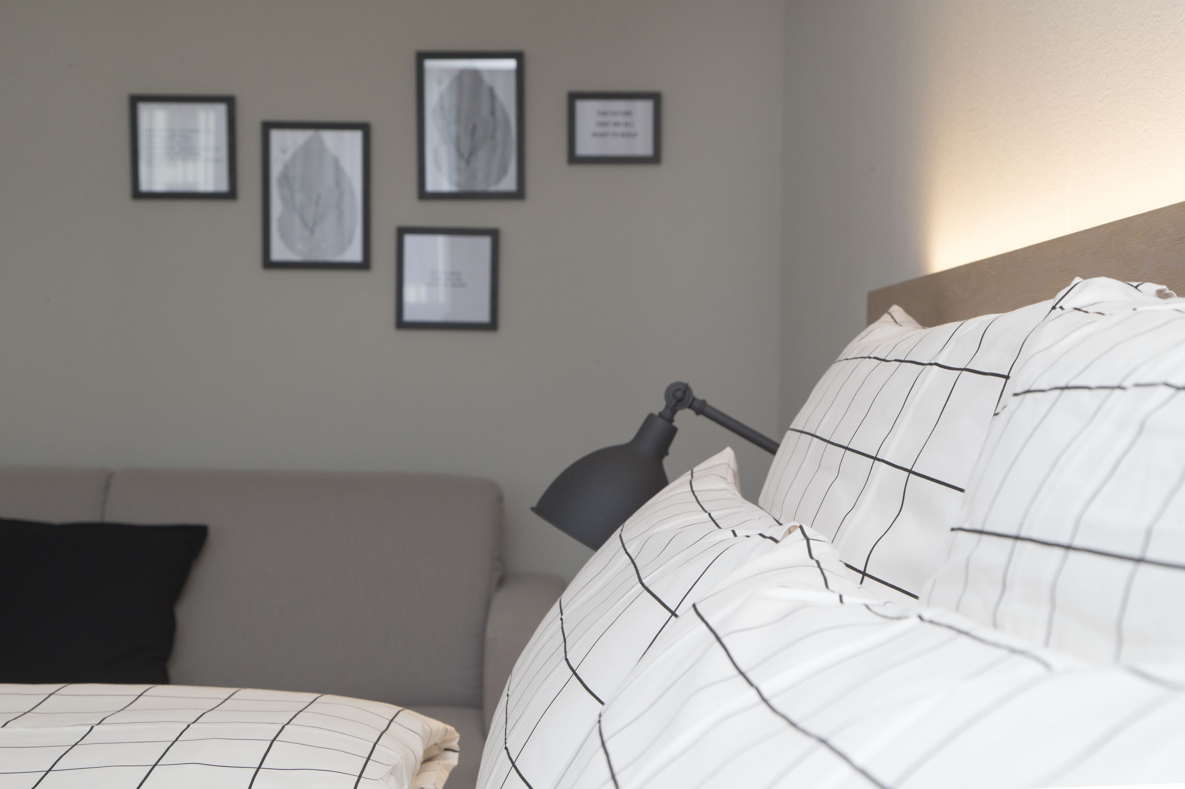 Une chambre à coucher avec un lit, une lampe de chevet, un canapé et des œuvres d’art encadrées accrochées au mur.