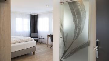 A modern hotel room with a bed, a small desk, a chair, and a glass door with a leaf design.