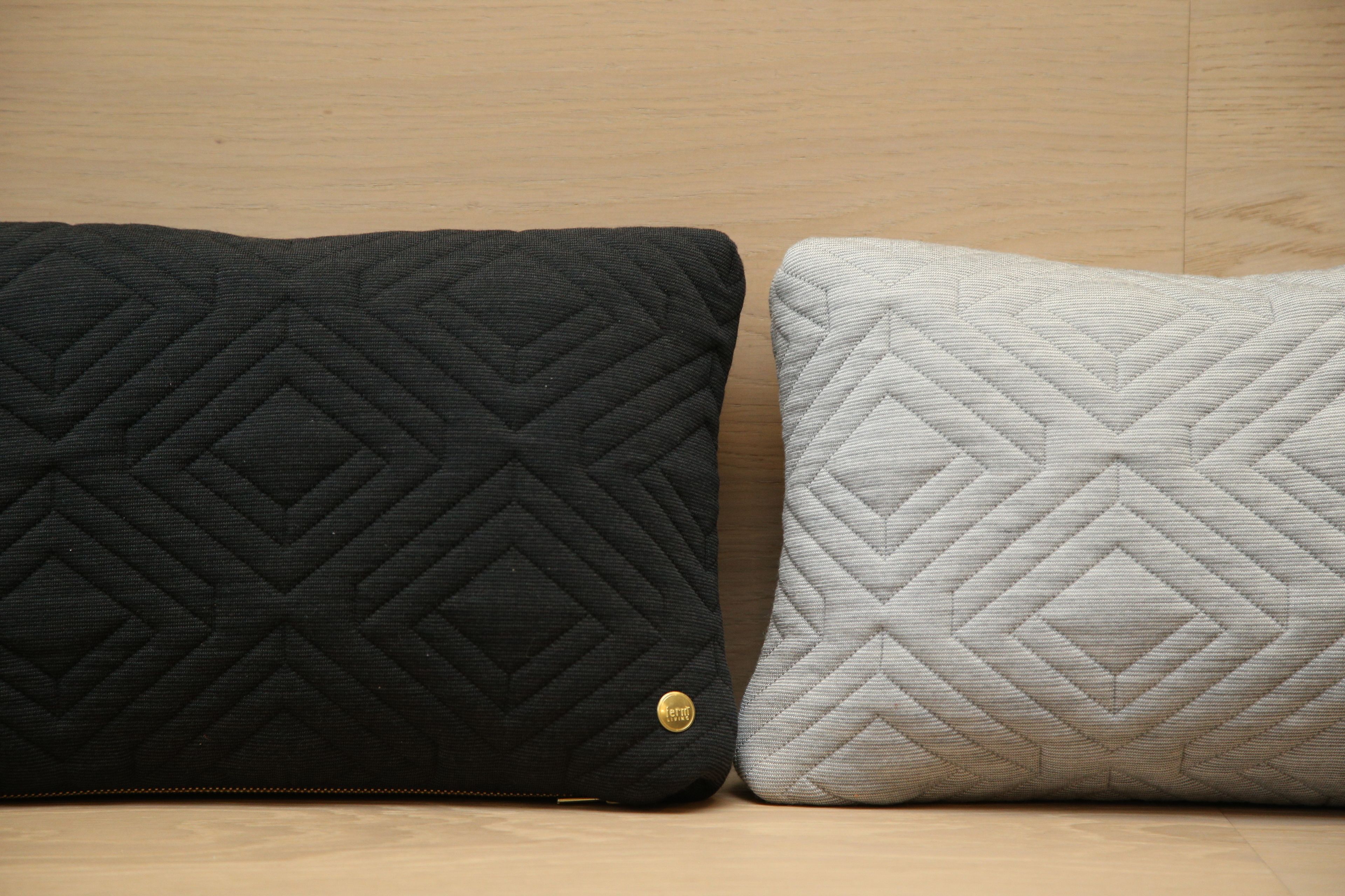 Dos almohadas con diseño de rombos, una negra y otra blanca, sobre una superficie de madera.