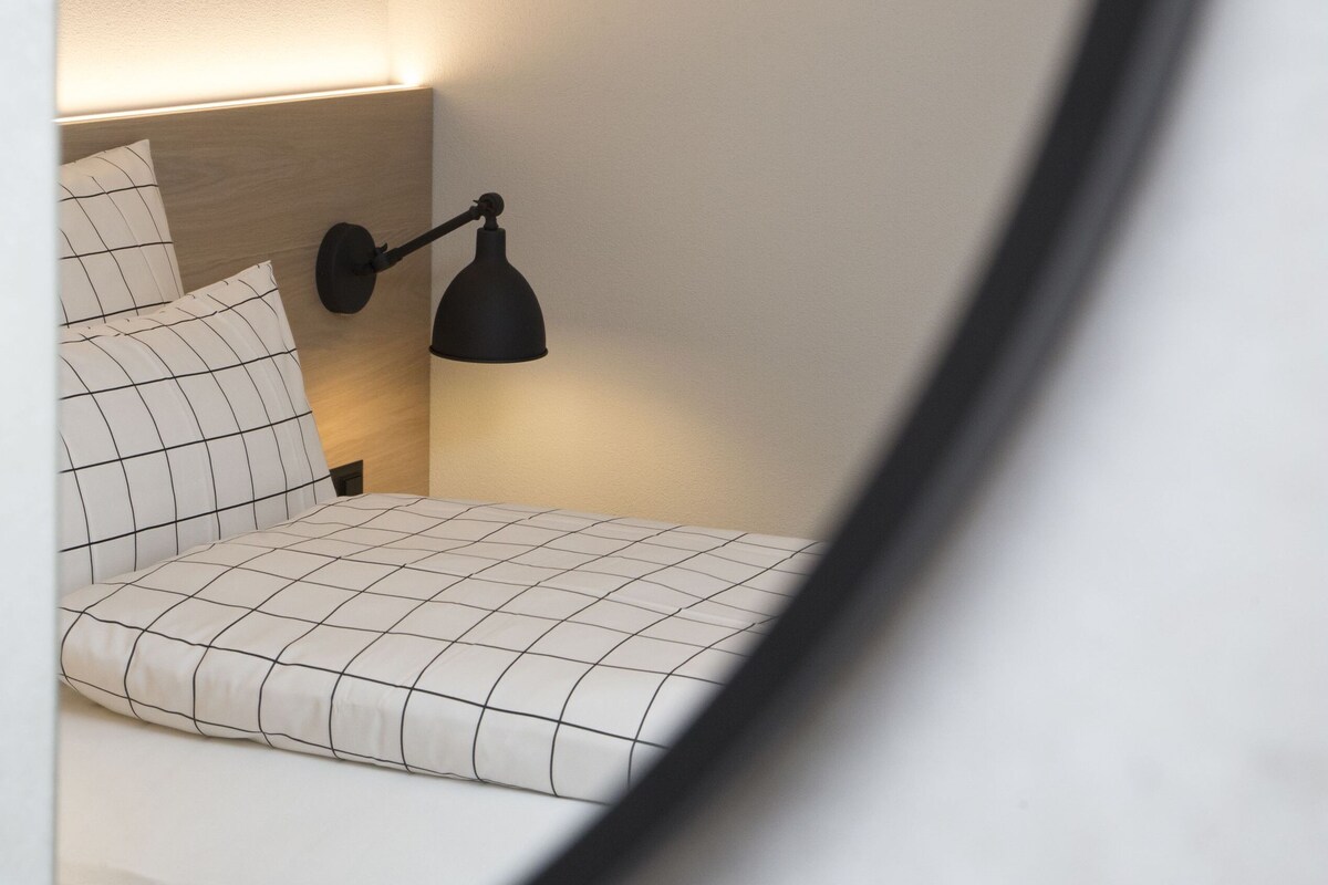 Ein Bett mit Kopfteil, eine Nachttischlampe und zwei gerahmte Bilder an der Wand.