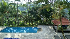 A swimming pool surrounded by lush greenery and a tiled deck. - The White Heron (Ubud)