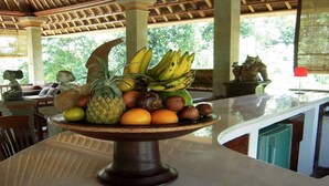 A fruit bowl on a table with a tropical ceiling and a view of greenery outside. - The White Heron (Ubud)