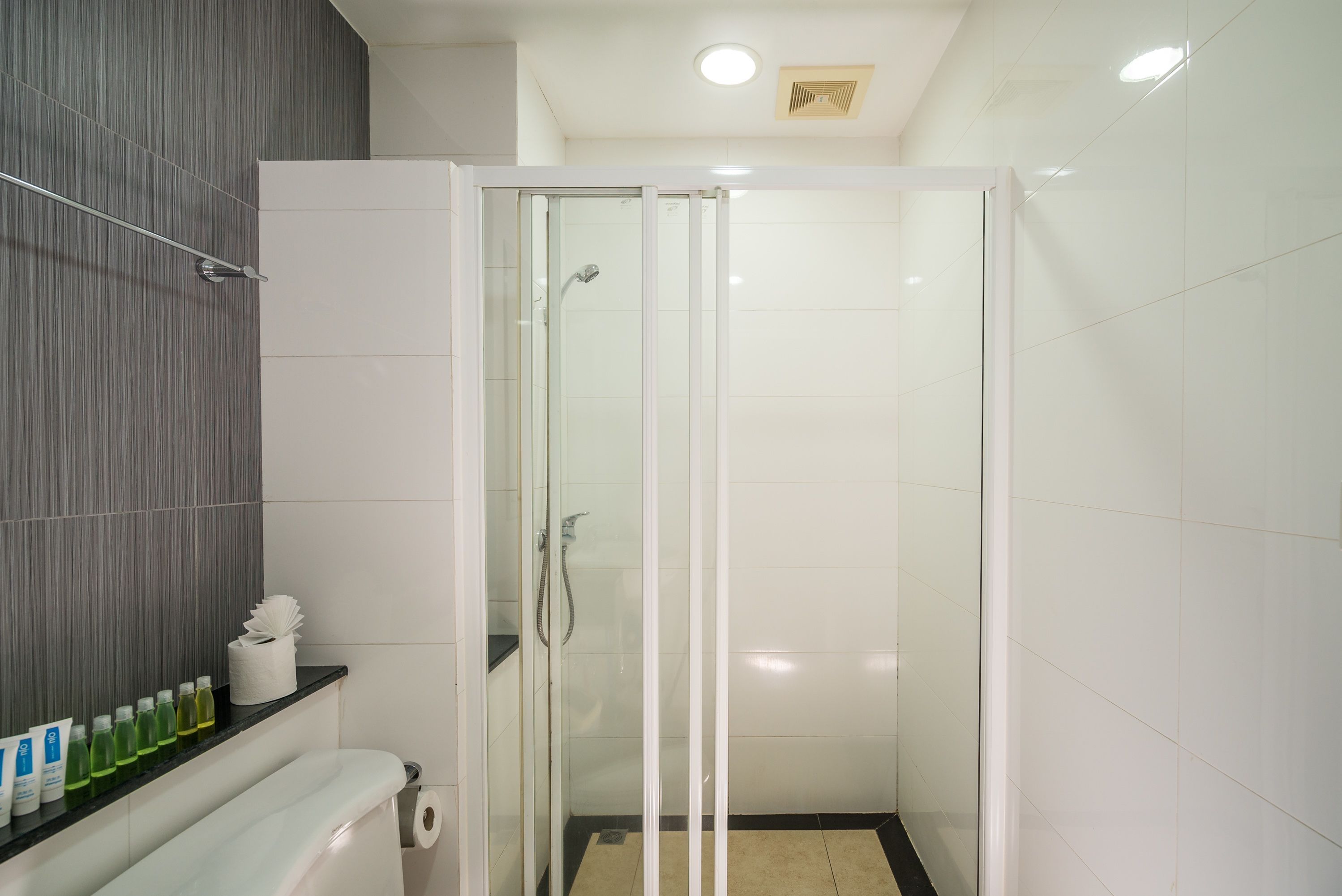 Un baño moderno con ducha de vidrio, tocador con artículos de aseo y perchero.