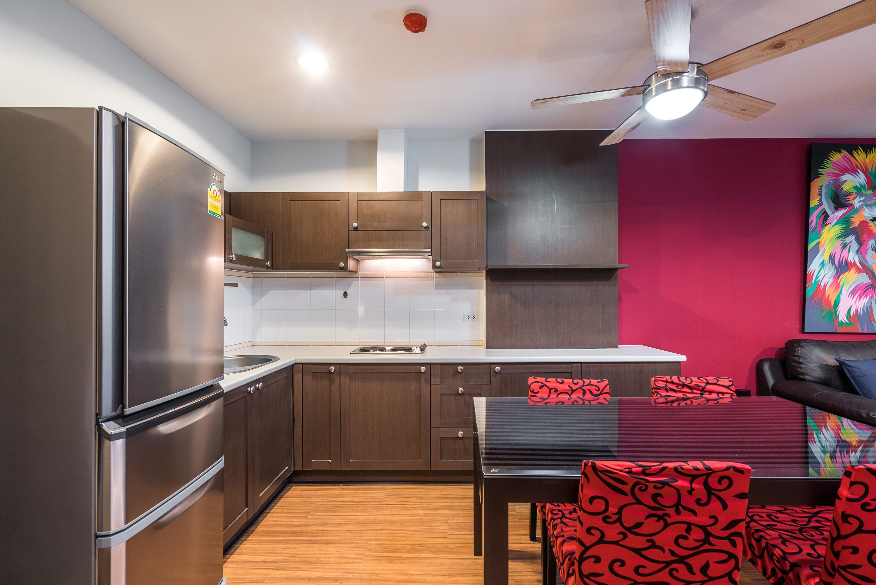 A modern kitchen with stainless steel appliances, wooden cabinets, and a dining area with red patterned chairs.