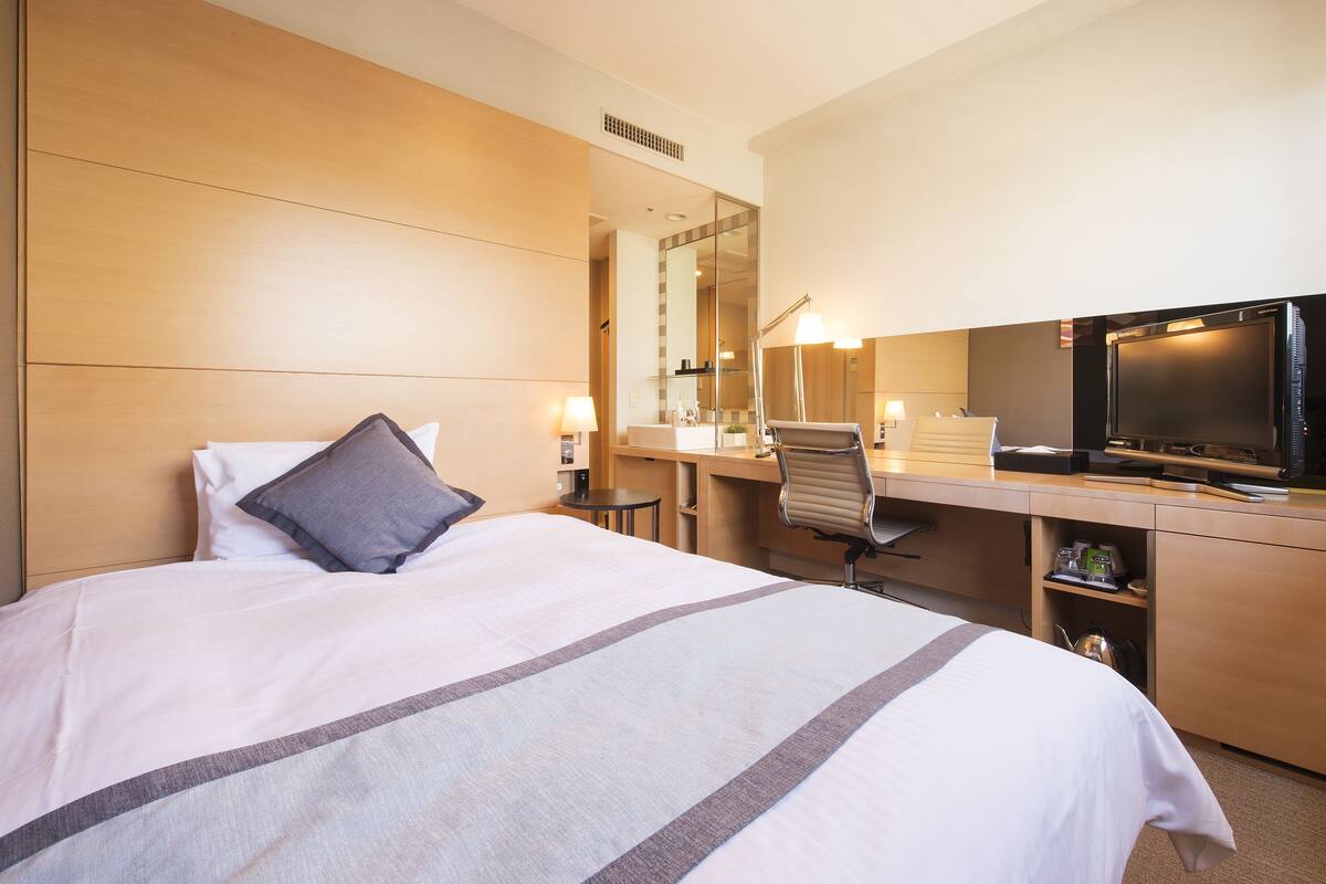 Een hotelkamer met een bed, een bureau, een stoel, een televisie en een spiegel.