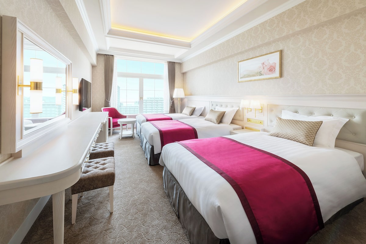 A hotel room with three beds, a desk, and a chair.