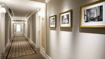 A long, narrow hallway with a patterned carpet, wall-mounted light fixtures, and framed black-and-white photographs.