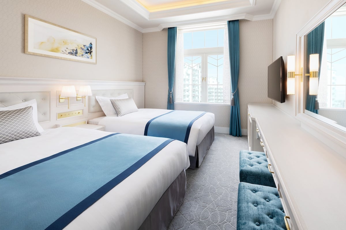 A hotel room with two beds, a large window with curtains, a flat-screen TV, and a painting on the wall.