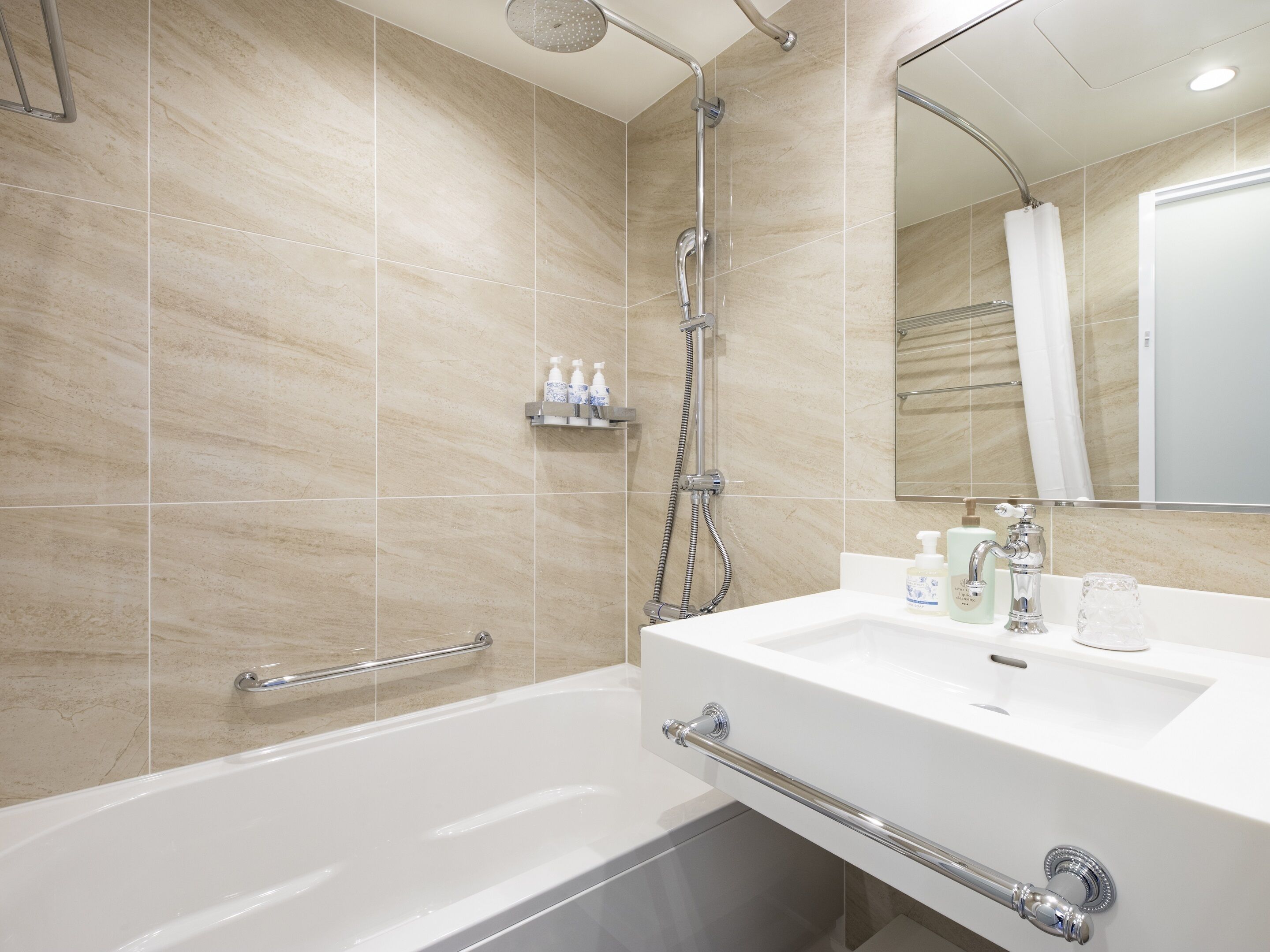 A modern bathroom with a bathtub, a shower, and a sink. There are handrails and a mirror above the sink.