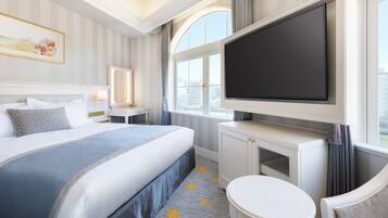 A hotel room with a large bed, a television mounted on the wall, a small table, and a chair.