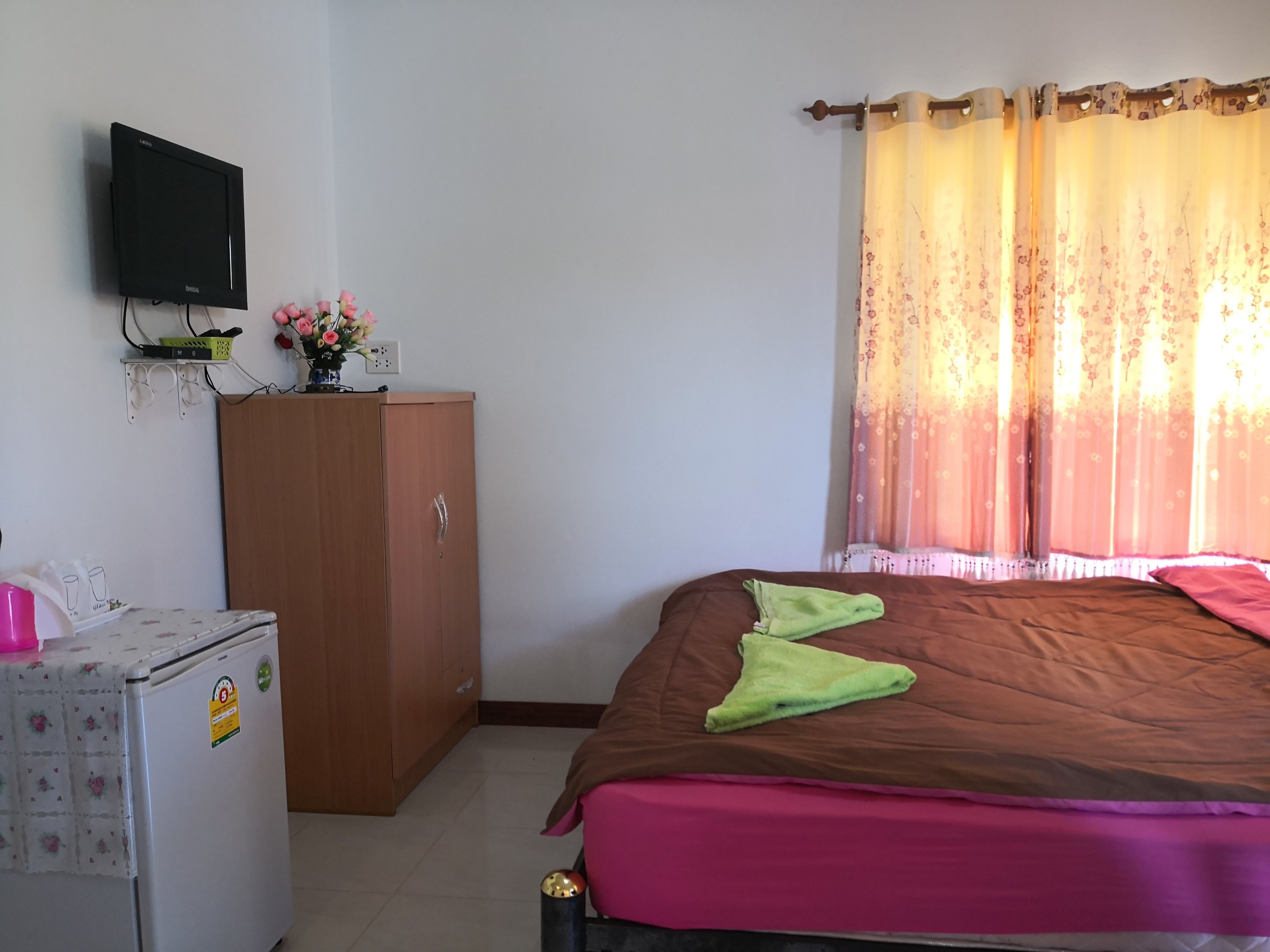 Un dormitorio con cama, armario, televisor montado en la pared y ventana con cortinas.