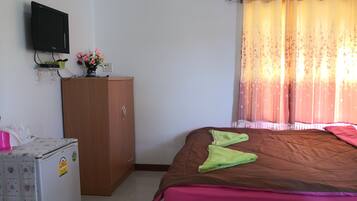 Un dormitorio con cama, armario, televisor montado en la pared y ventana con cortinas.