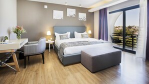A modern hotel room with a large bed, a desk, a chair, and a balcony with a view.