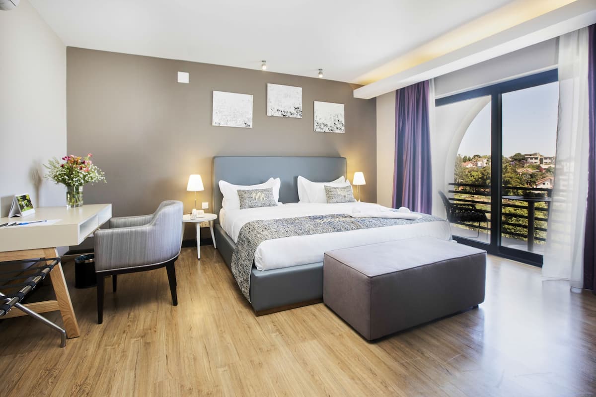 Habitación de hotel moderna con una cama grande, un escritorio, una silla y un balcón con vistas.