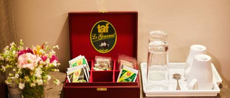 Una caja roja con un logotipo, una bandeja con una jarra de vidrio, vasos y una cuchara, y un florero con flores.