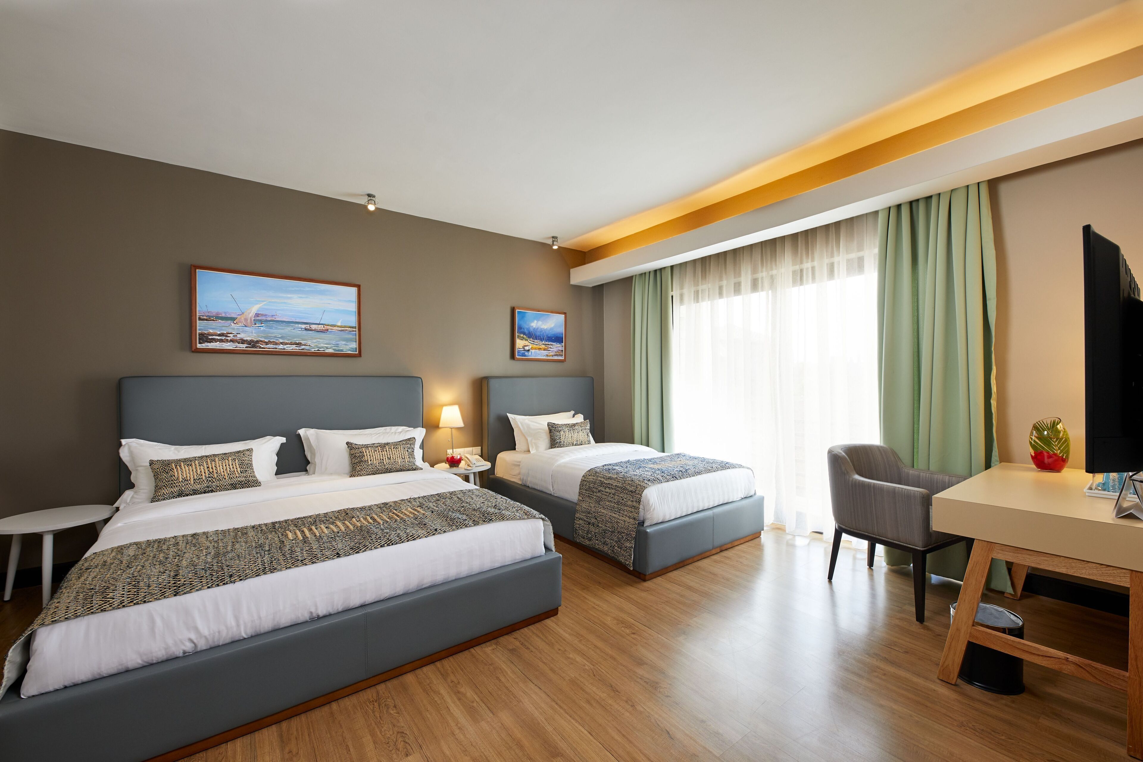 A hotel room with two beds, a desk, a chair, and a TV.