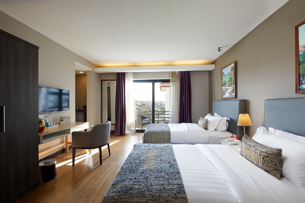 Habitación de hotel con televisión, escritorio, dos camas, una silla y vista al balcón.