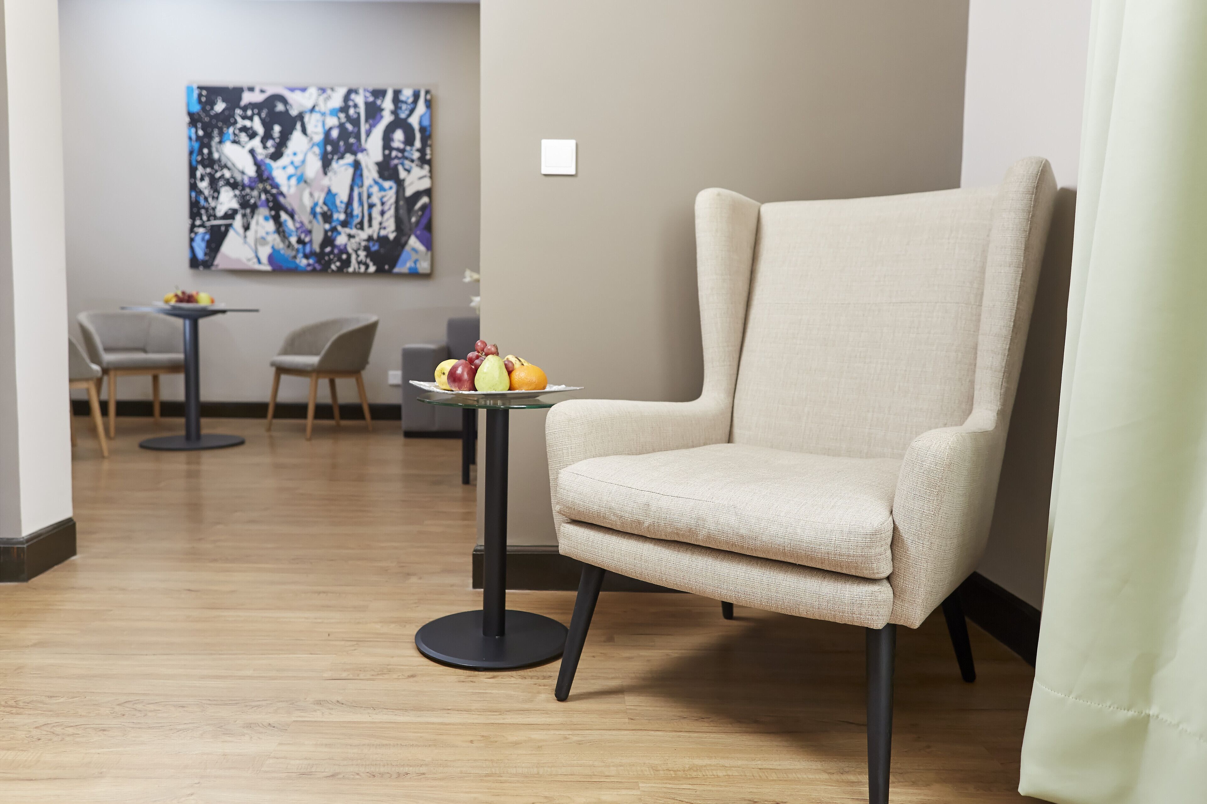 A modern room with a beige armchair, a small round table with fruit, and a painting on the wall.