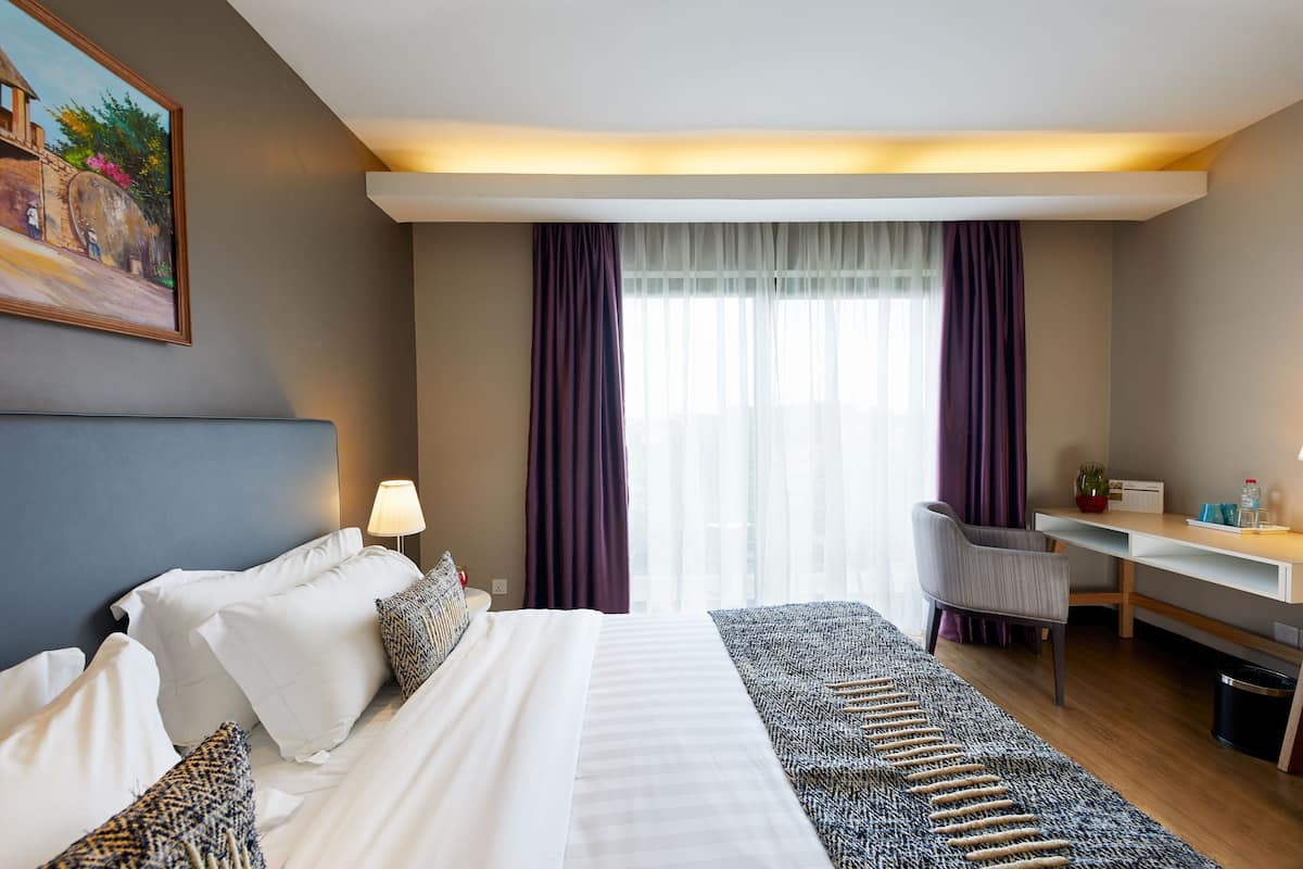 Una habitación de hotel con cama, escritorio, silla y un cuadro en la pared.