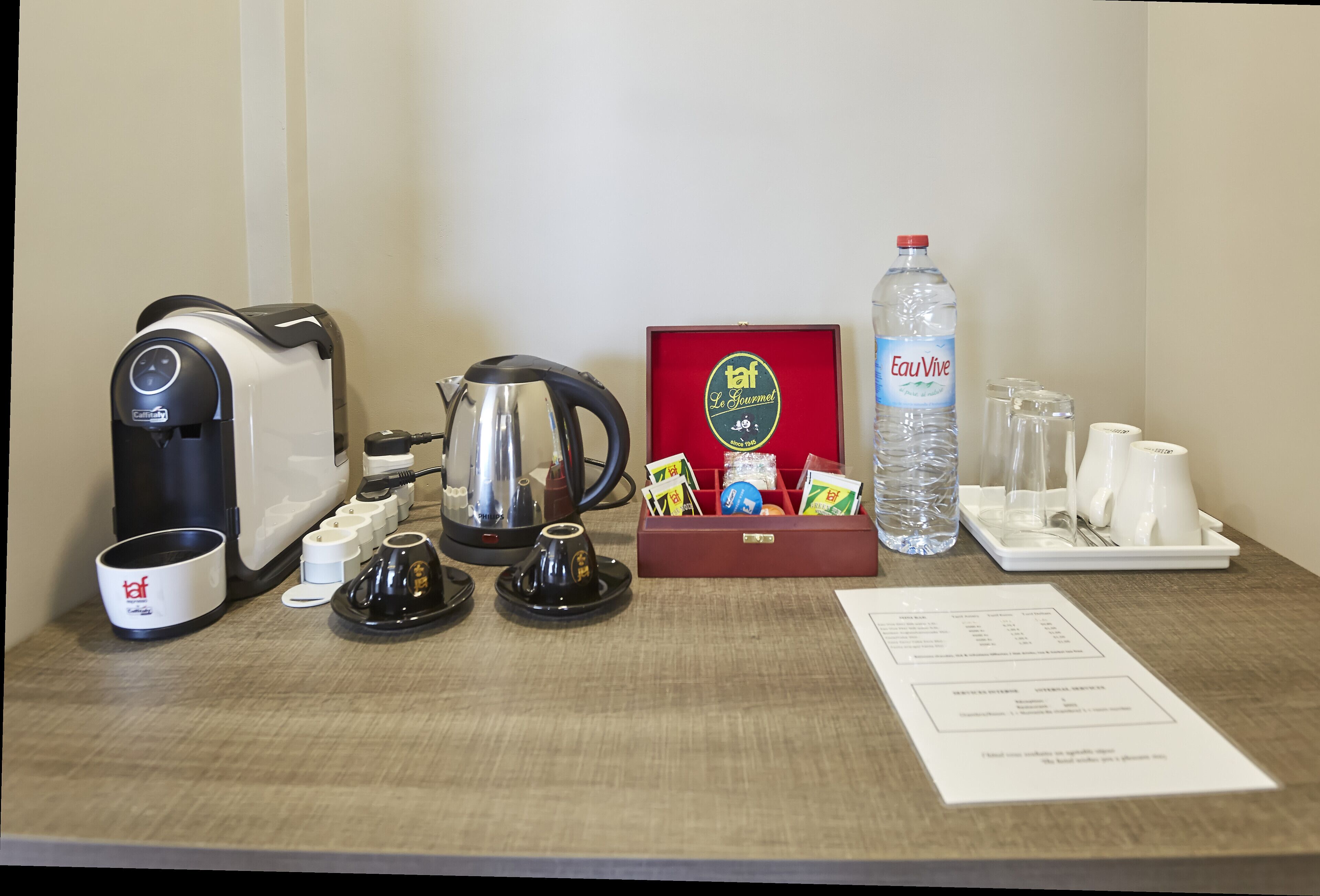 Ontbijtsetup in een hotelkamer, met koffiezetapparaat, waterkoker, theezakjes, waterfles en theekoppen.