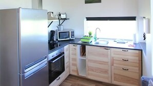 A compact kitchen with a refrigerator, microwave, and stove. There is a window above the sink and a painting on the wall. - Blue View Cabin 1A with Hot Tub (Bláskógabyggd)