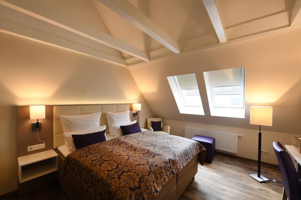 A bedroom with a large bed, two bedside tables, a nightstand, a floor lamp, and a window with a view.