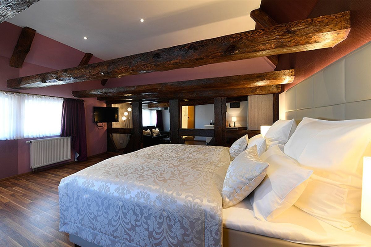 Une chambre avec un grand lit, des poutres en bois, une télévision et une fenêtre avec des rideaux.