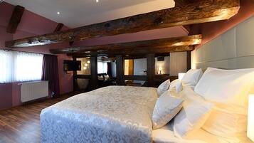 A bedroom with a large bed, wooden beams, a television, and a window with curtains.