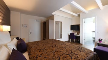 Habitación de hotel con una cama grande, un escritorio, una silla, un televisor y una puerta que da a otra habitación.