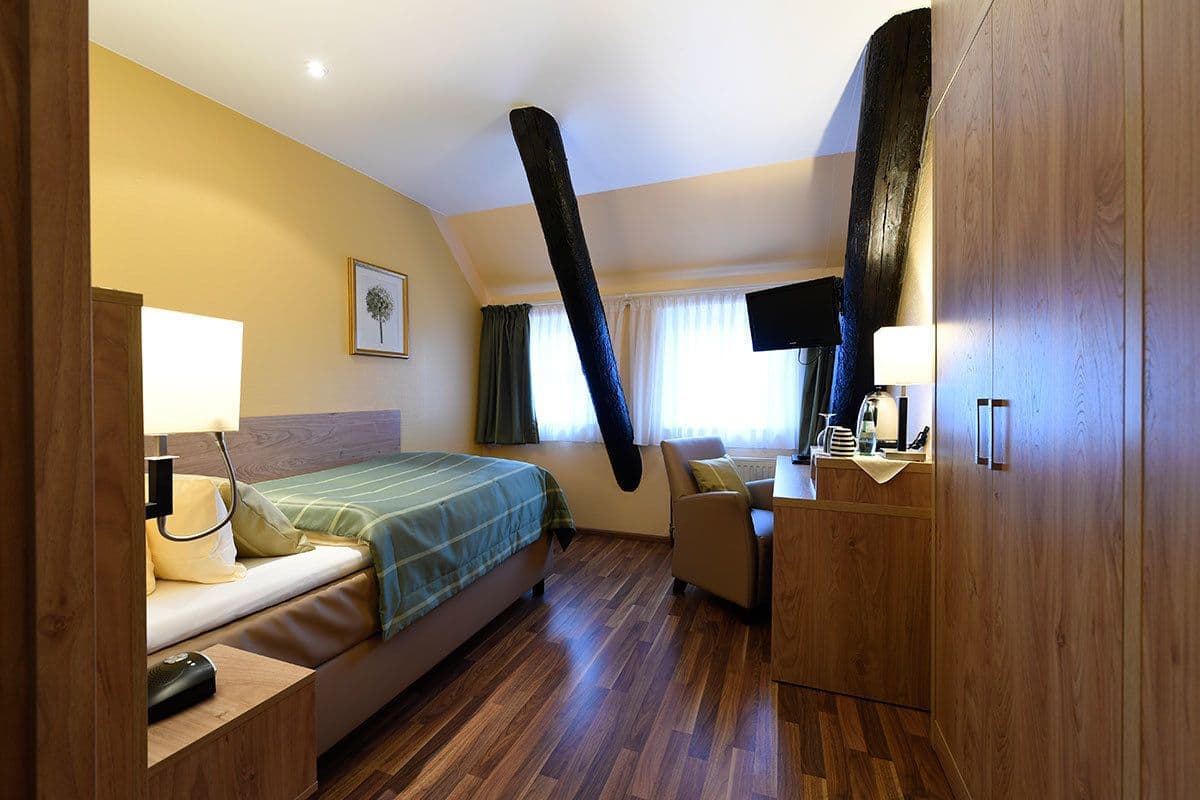 A hotel room with a bed, bedside table, lamp, chair, and a large mirror.