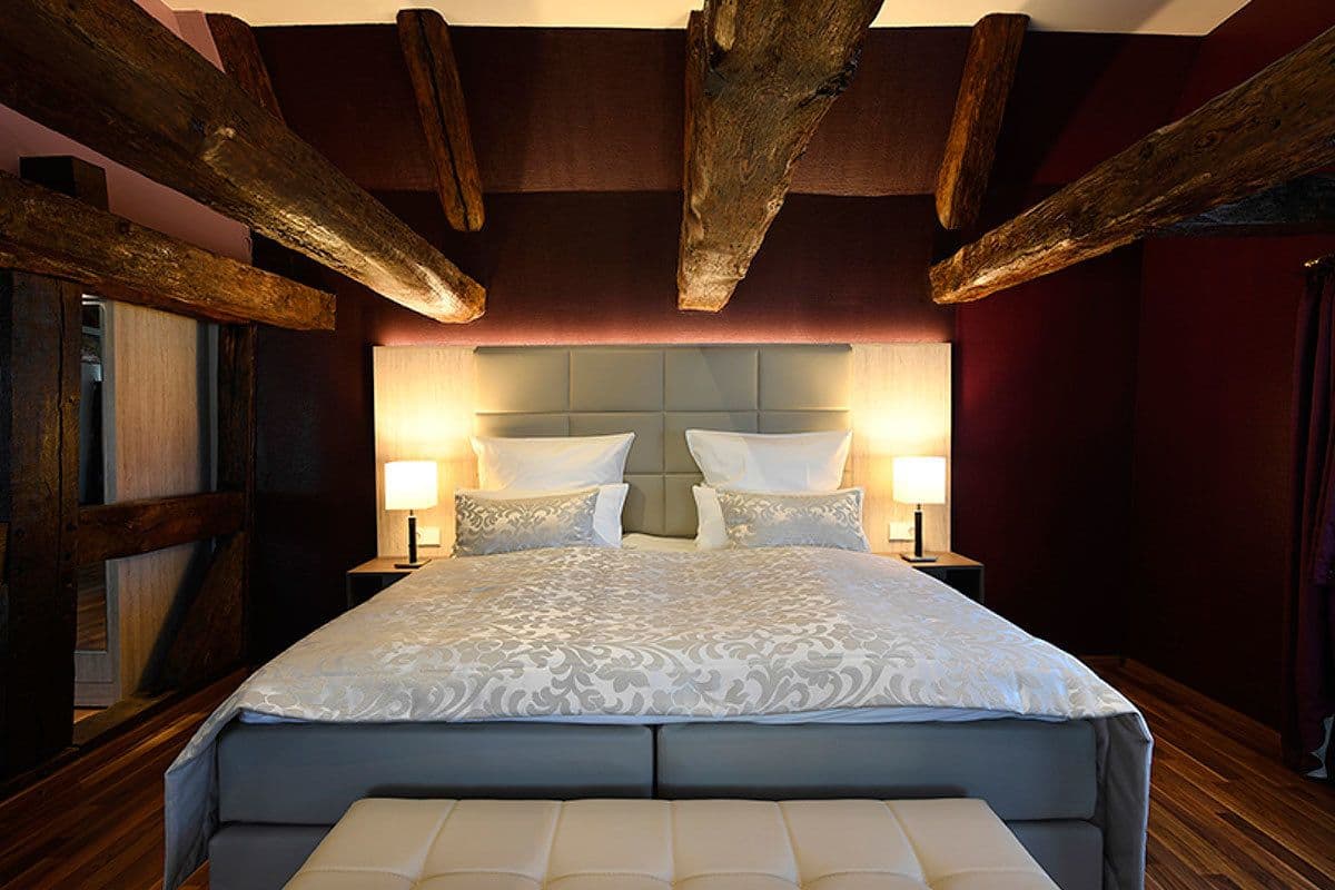 A large bed with a tufted headboard, two bedside lamps, and a wooden ceiling structure.