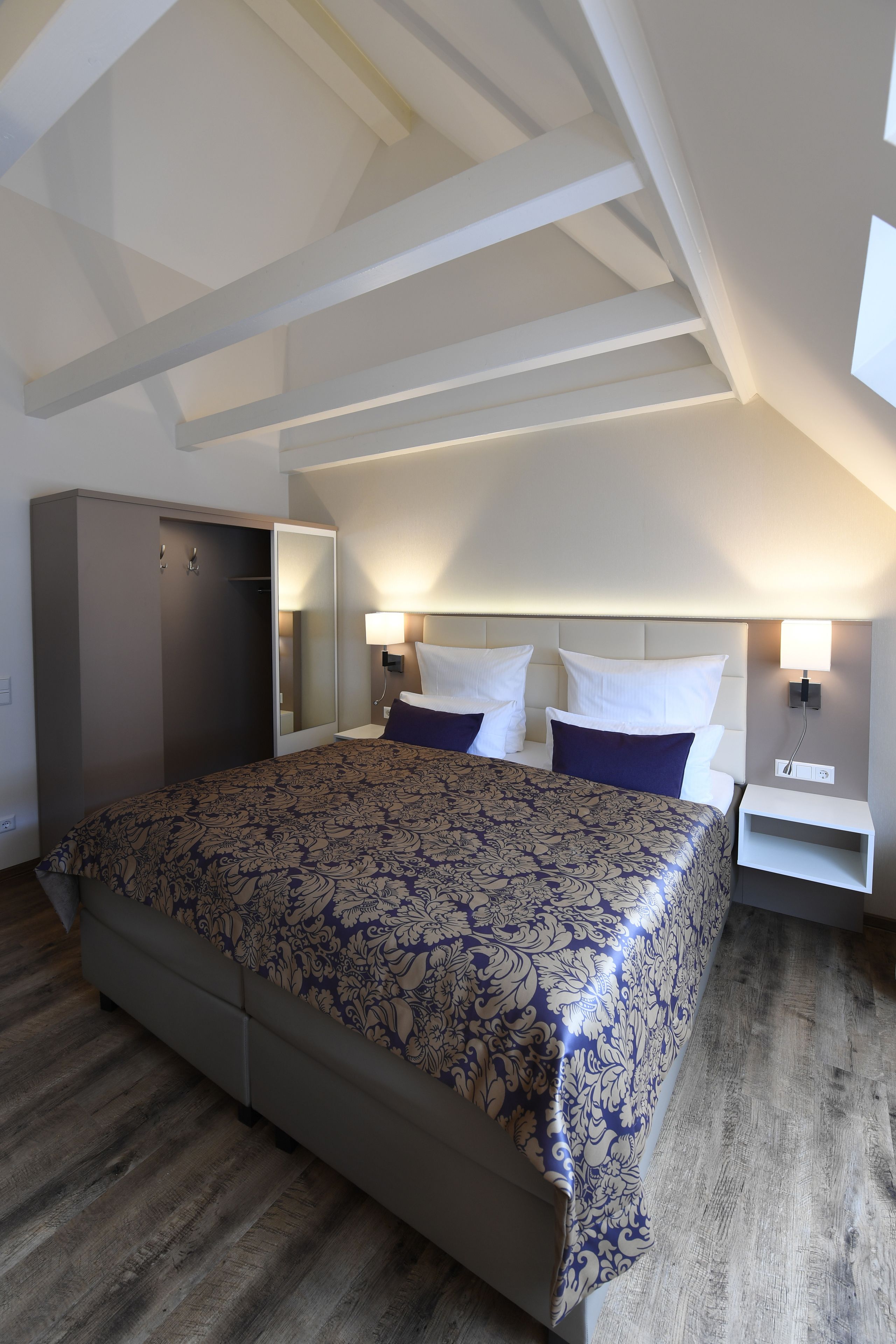 Ein Schlafzimmer mit einem großen Bett, einem Kleiderschrank, einem Nachttisch mit Lampe und einem Himmel mit Dachfenstern.
