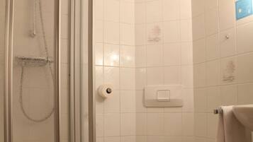 Un baño con ducha de vidrio, inodoro y un taburete blanco pequeño.
