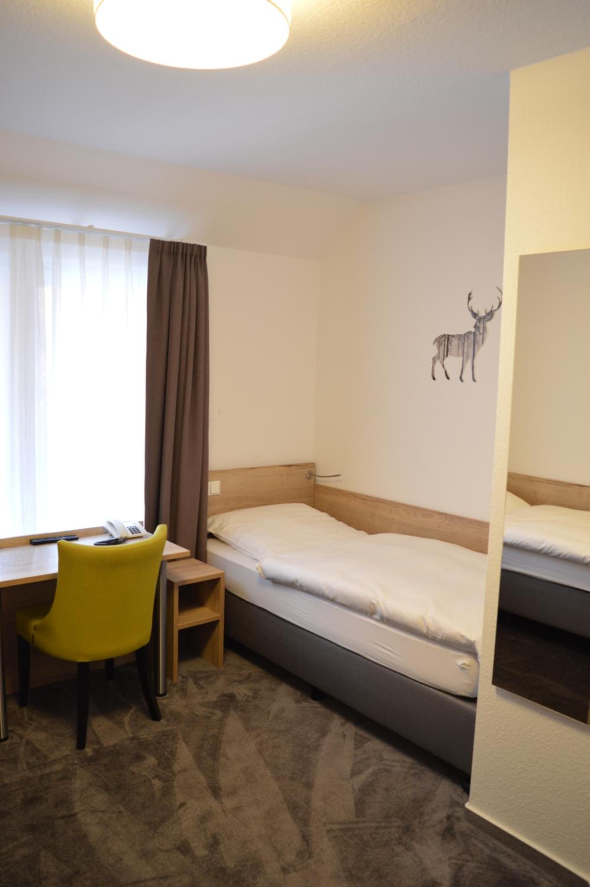 Hotelkamer met een bed, bureau met stoel, telefoon en een muurdecoratie van een hert.