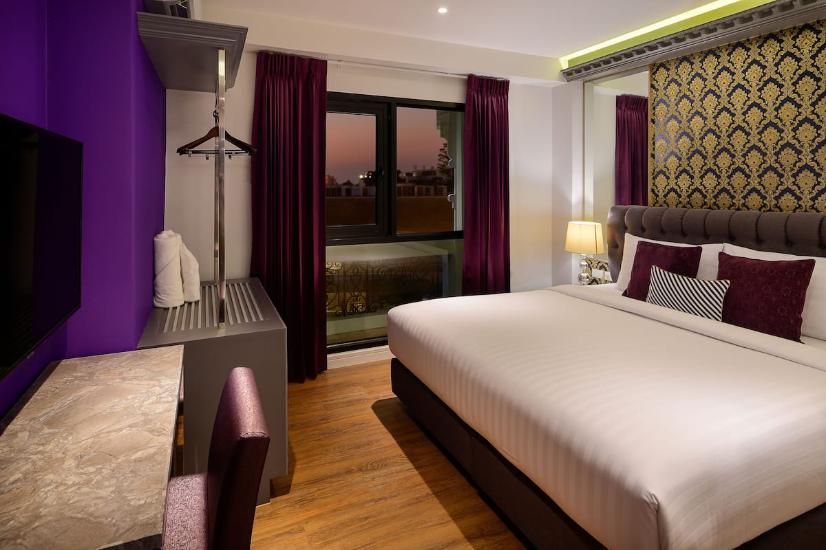 A hotel room with a bed, a desk, a chair, a window with curtains, and a view of the outside.