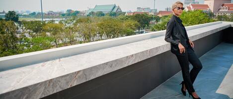 Una persona parada en una terraza en la azotea, con un paisaje urbano de fondo.