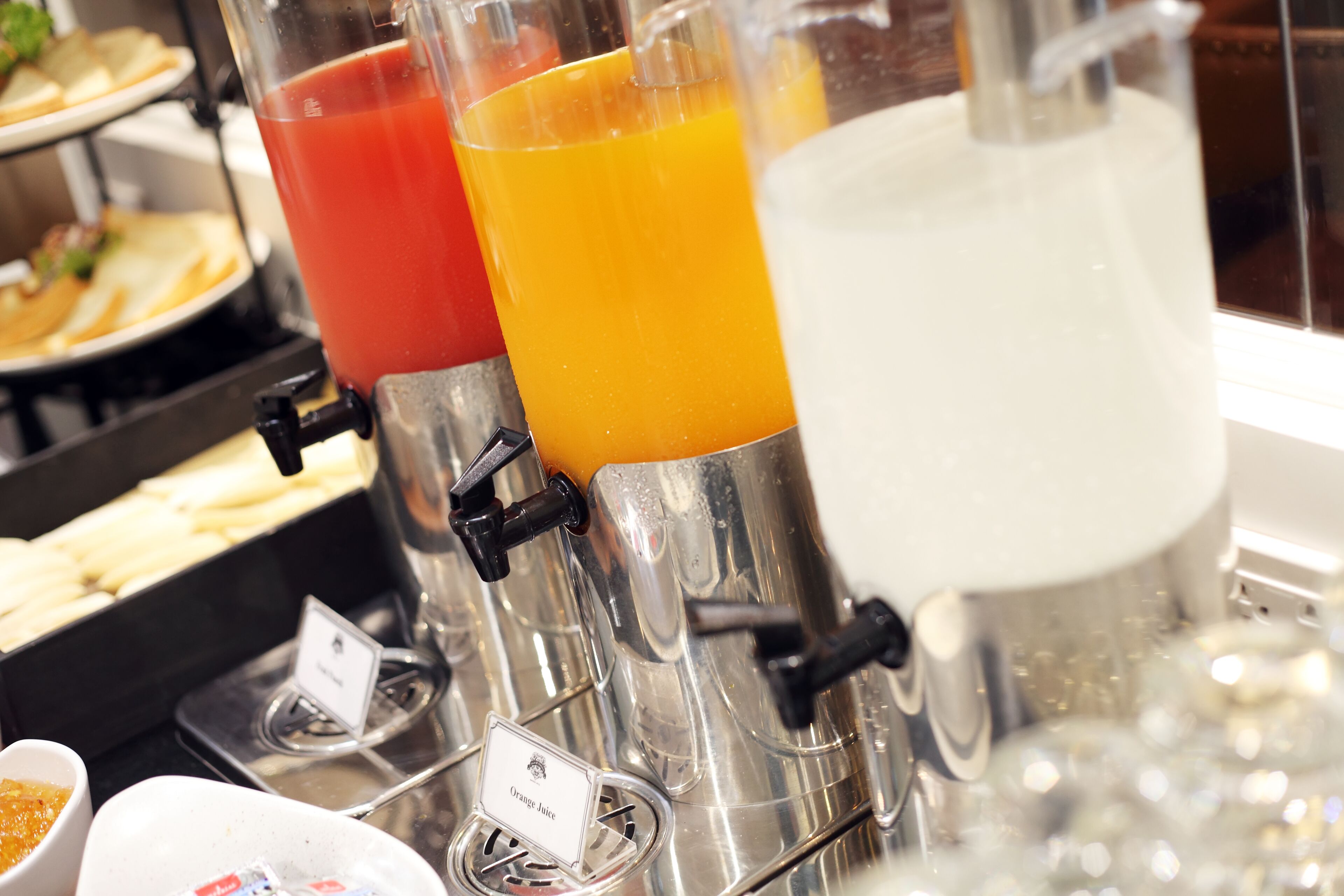 A juice dispenser with three different colored liquids, a small bowl with a condiment, and a sign indicating the type of juice.