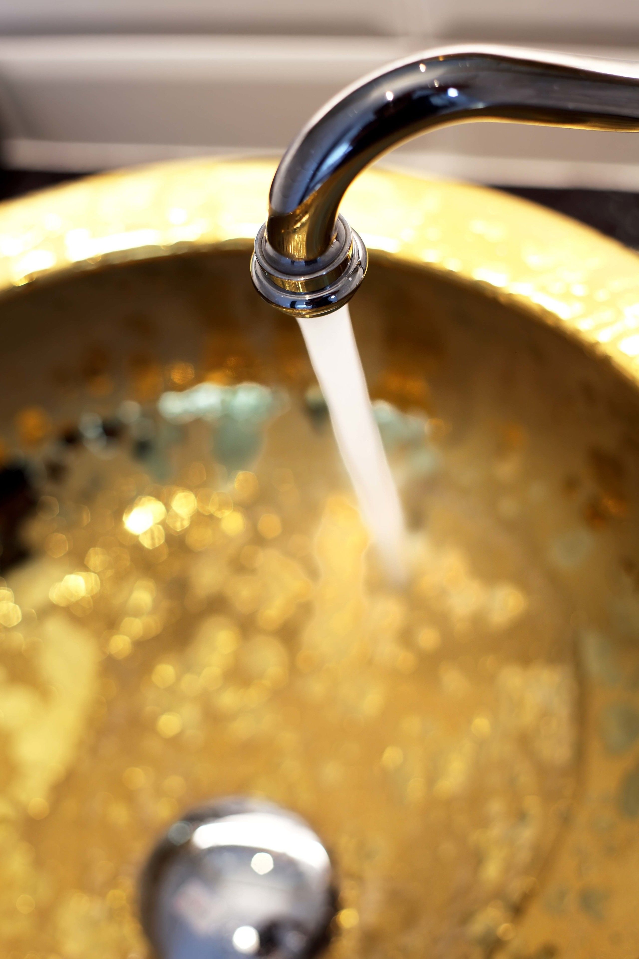 A close-up of a faucet with water flowing into a golden basin.