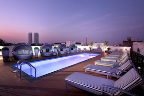 Zona de piscina en la azotea con sillas reclinables y asientos, rodeada de edificios modernos.