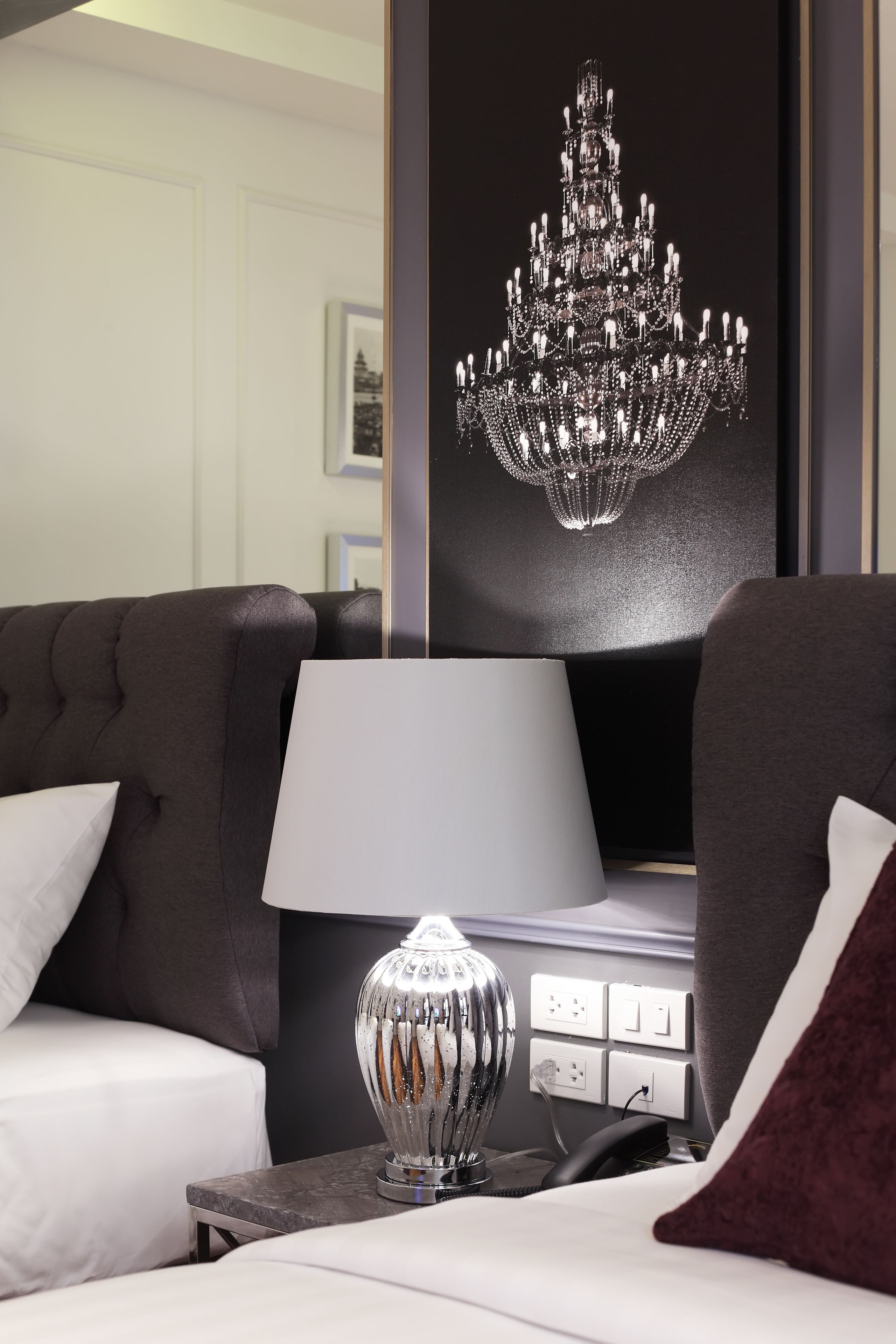 Habitación de hotel moderna con un sofá de color oscuro, una mesita de noche blanca con lámpara y una obra de arte con un candelabro enmarcado en la pared.